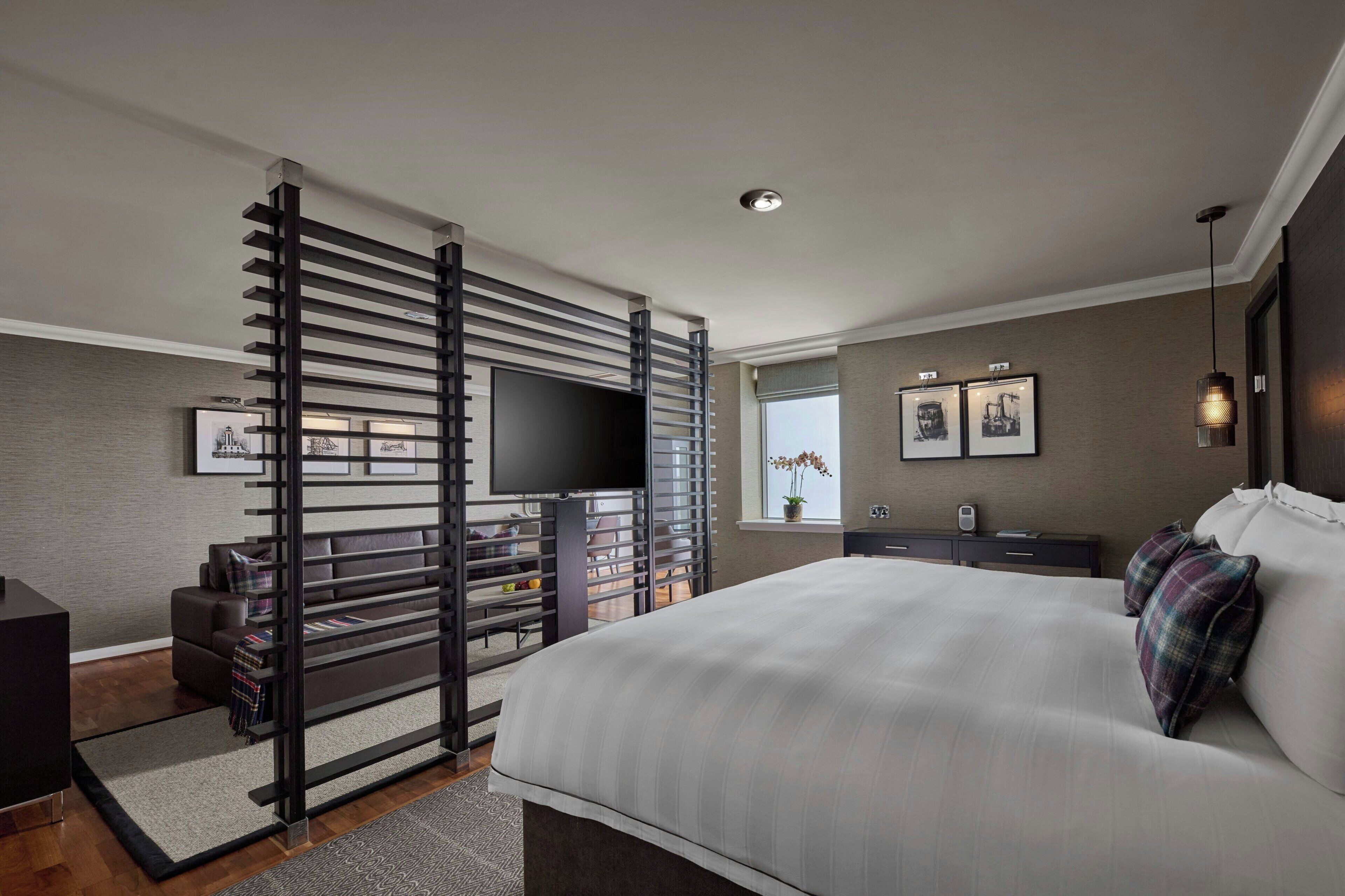 A modern bedroom with a large bed, a TV, a desk, and a window with a view.