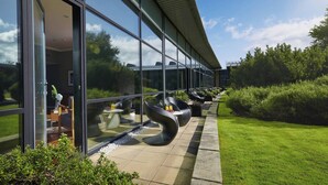 A modern building with large glass windows, outdoor seating with chairs and tables, and a well-maintained lawn. - The Glasshouse, Autograph Collection (Edinburgh)