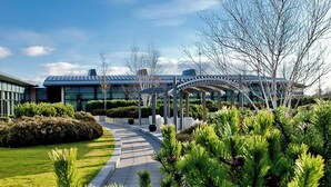 A modern building with a glass facade, surrounded by well-maintained greenery and a clear sky. - The Glasshouse, Autograph Collection (Edinburgh)