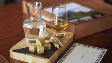 A wooden board with a bottle of water, a glass of whiskey, and some cheese cubes on a table.