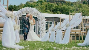 A wedding ceremony with a white floral arch and guests seated on wooden chairs. - The Glasshouse, Autograph Collection (Edinburgh)