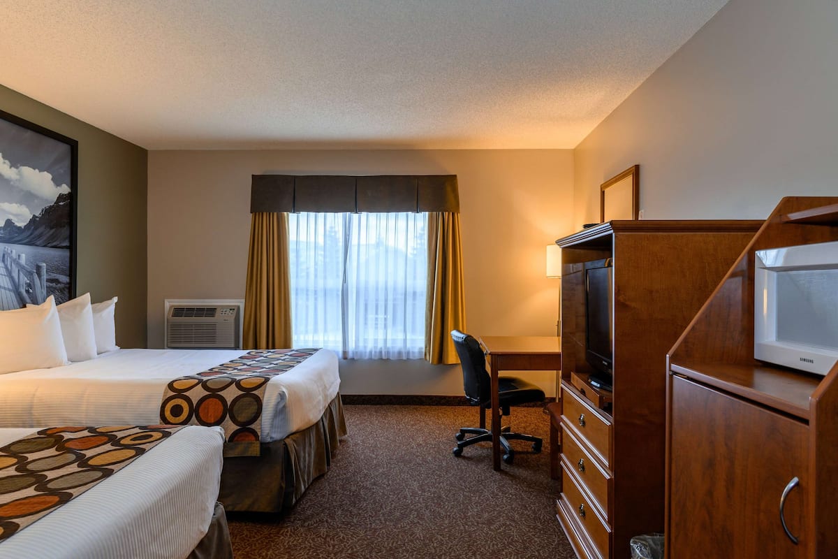 A hotel room with two beds, a desk, a television, and a cabinet.