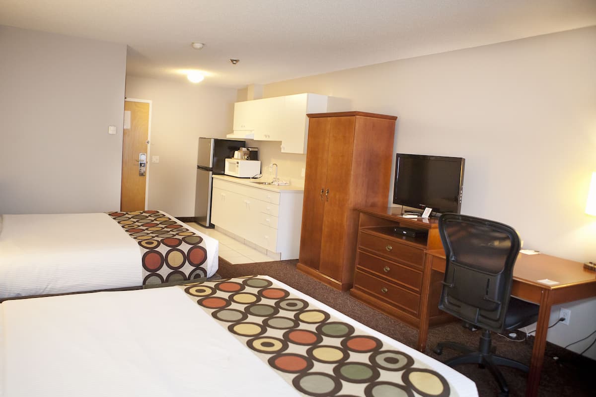 A hotel room with two beds, a desk, a television, and a kitchenette.