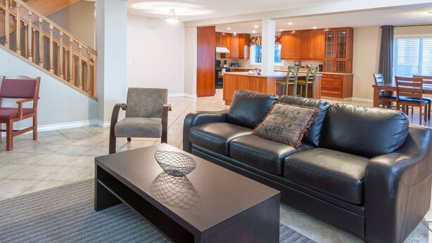 A modern living room with a leather sofa, a coffee table, and a dining area with wooden furniture. - Super 8 by Wyndham Cochrane (Cochrane)