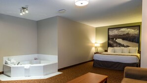 A hotel room with a large bathtub, a bed with a green wall, a lamp, and a painting of a mountain landscape. - Super 8 by Wyndham Cochrane (Cochrane)