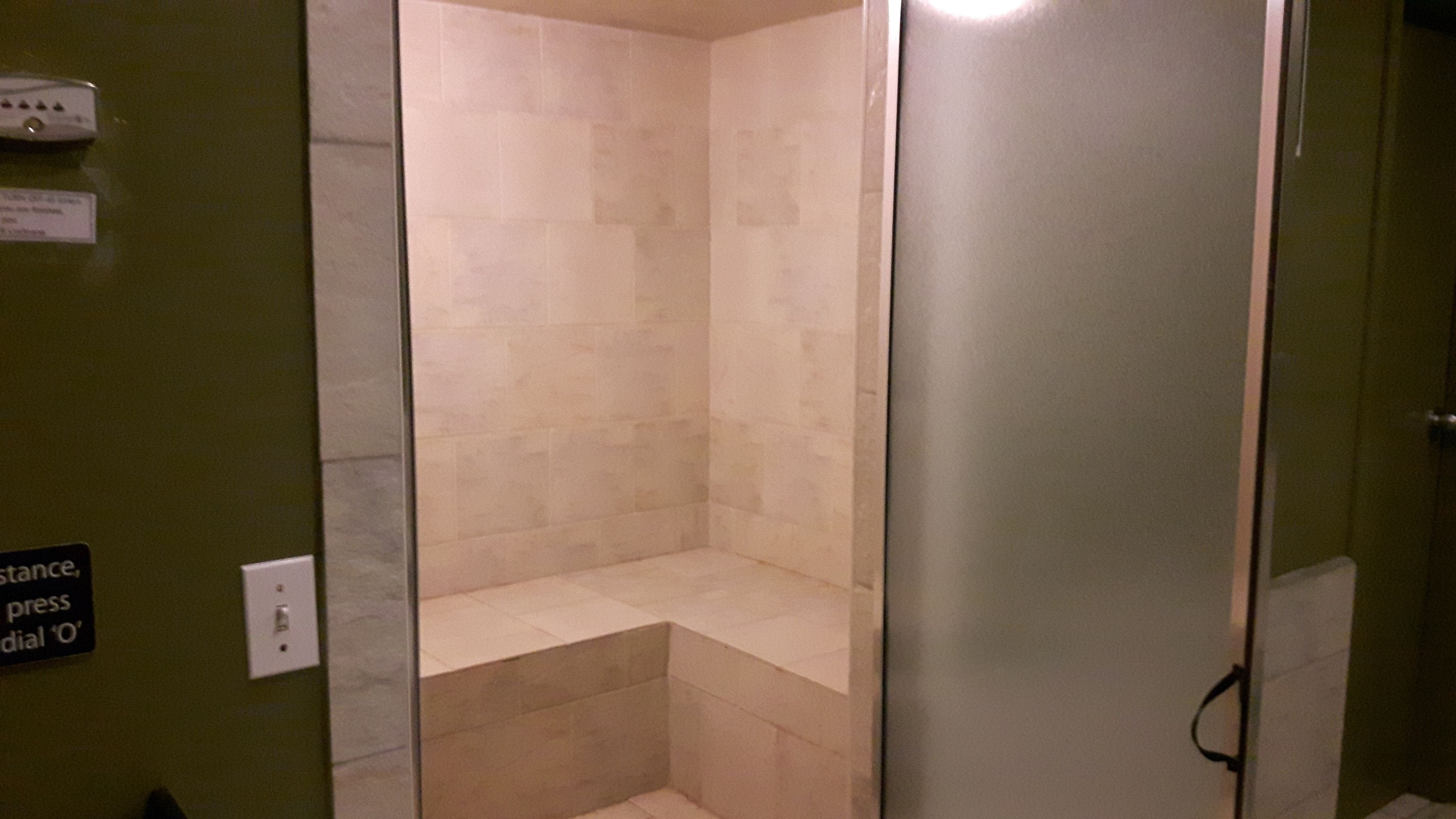 A small, enclosed shower area with a tiled wall and a bench.