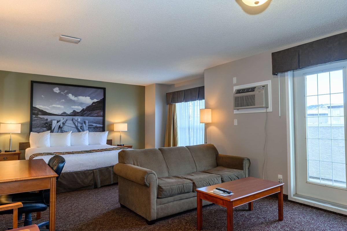 A hotel room with a bed, a sofa, a desk, and a window with a view.