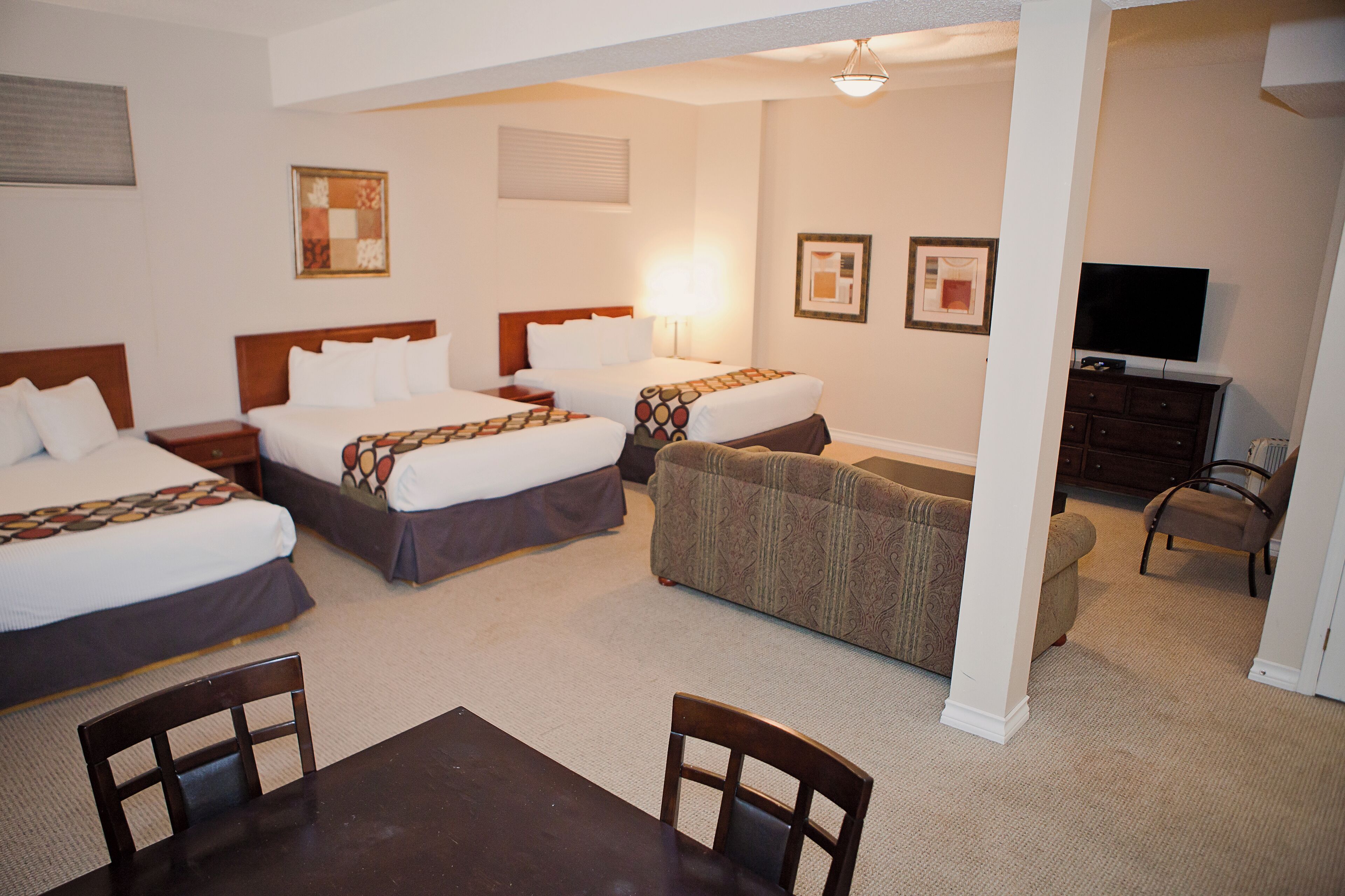 A hotel room with two beds, a sofa, a TV, and a dining area.