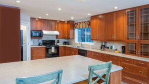 A kitchen with wooden cabinets, a large island with two chairs, a microwave, stove, and various appliances. - Super 8 by Wyndham Cochrane (Cochrane)
