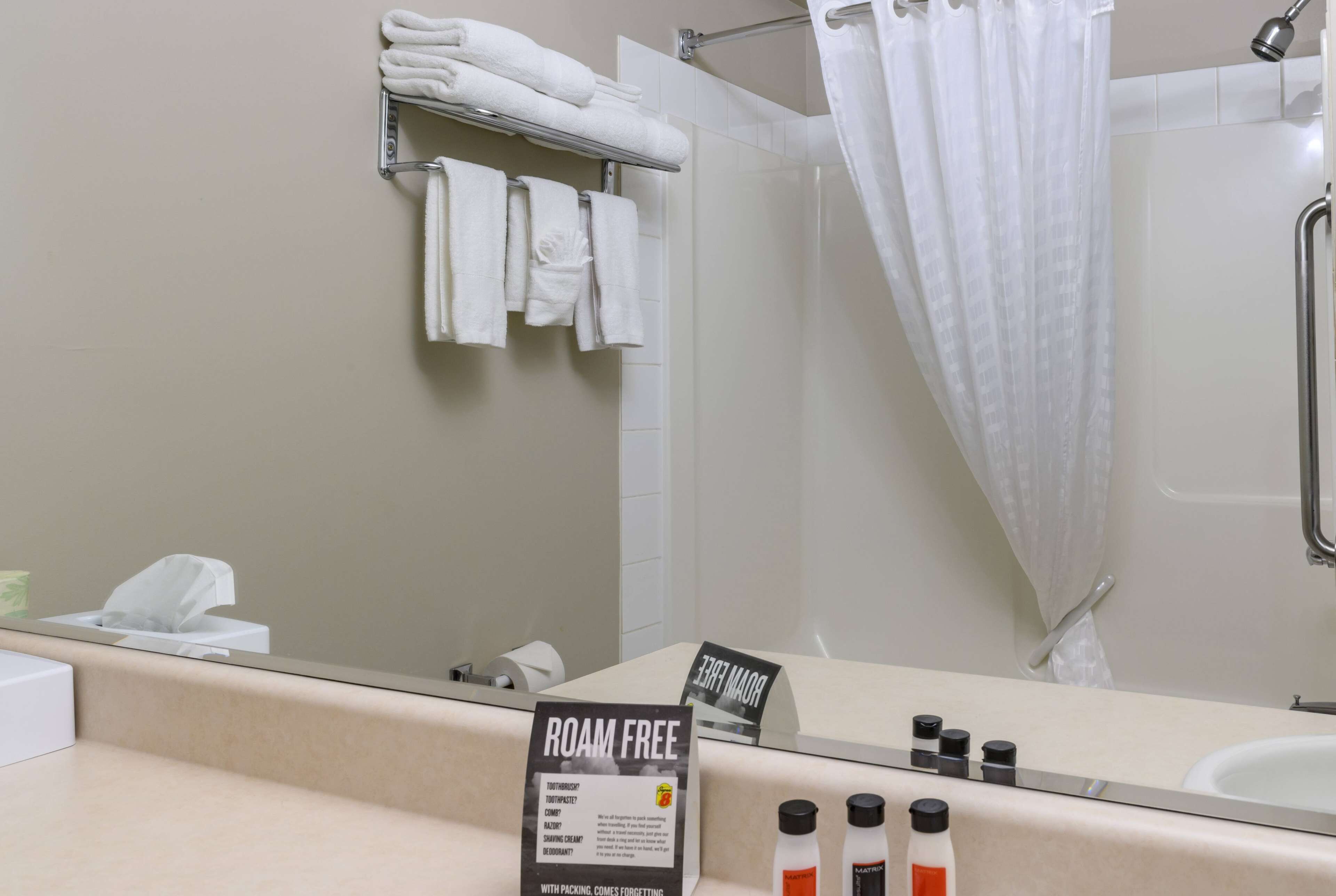 A bathroom with a mirror, a towel rack with folded towels, a shower curtain, and a sign indicating the room is 'ROOM FREE'.