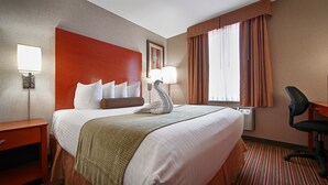 Habitación de hotel con una cama grande, un escritorio, una silla, una lámpara de pared y una ventana con cortinas.