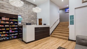 Zona de recepción con una escalera de madera, mostrador de recepción y televisor montado en la pared.