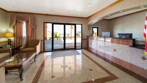 Un vestíbulo de hotel con mostrador de recepción, un sofá, una mesa de centro y un amplio ventanal con cortinas.