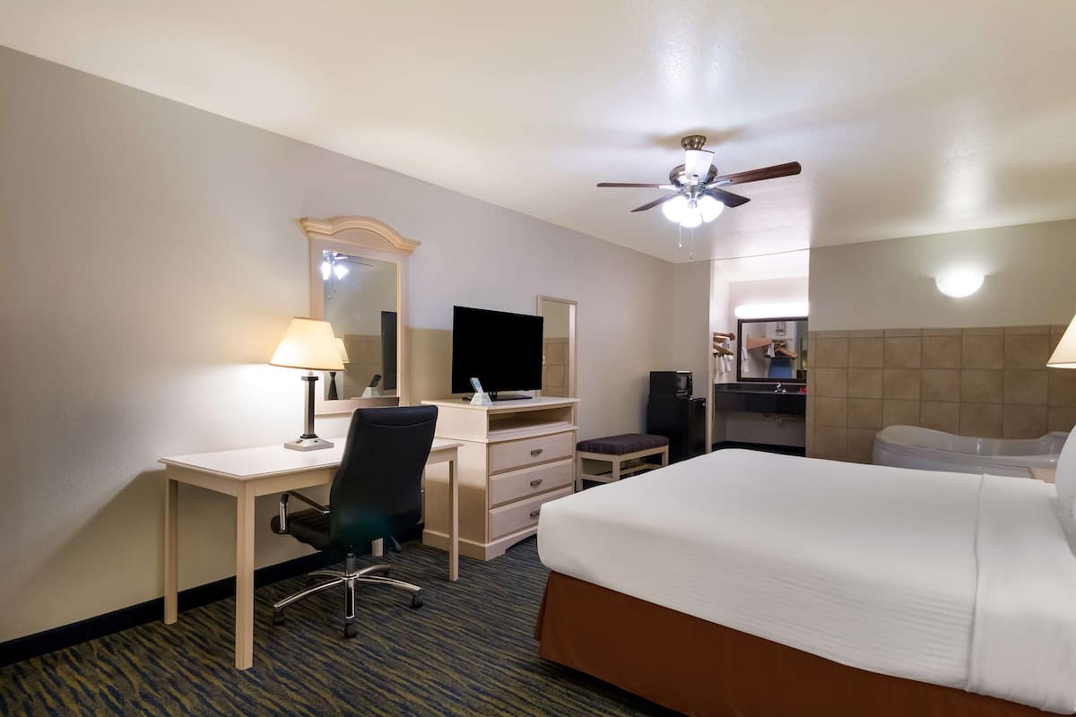 A hotel room with a bed, desk, chair, dresser, and a ceiling fan.