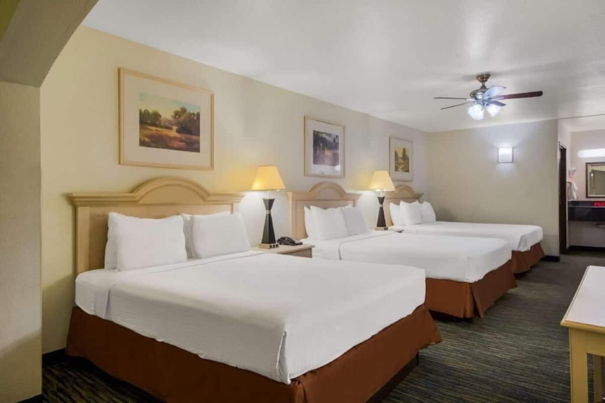 A hotel room with three beds, a ceiling fan, and framed pictures on the wall.