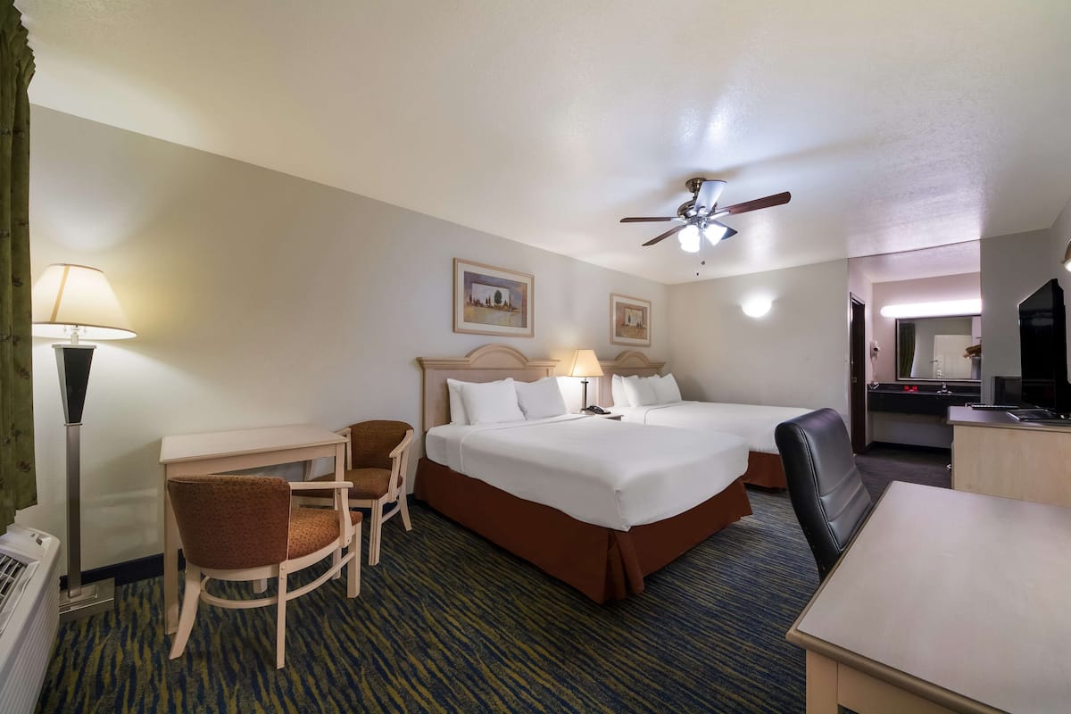 A hotel room with a large bed, two bedside tables, a desk, a chair, a ceiling fan, and a lamp.