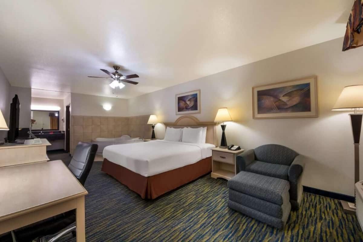A hotel room with a bed, desk, chair, and a ceiling fan.