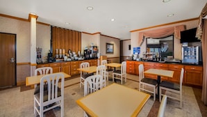 Un comedor de hotel con mesas y sillas de madera, una estación de café y un refrigerador.