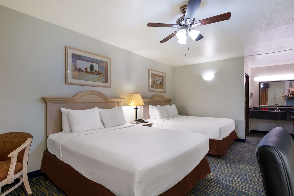 A hotel room with two beds, a ceiling fan, a desk with a lamp, and a bathroom visible through an open door.