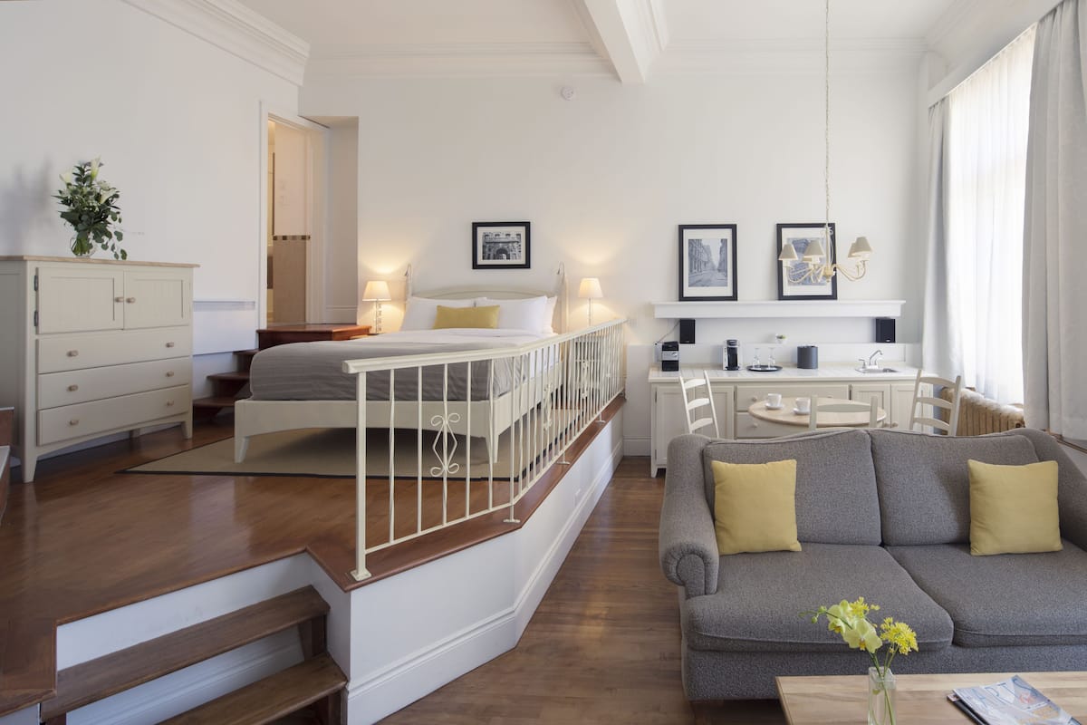 A modern hotel room with a bed, sofa, dining area, and staircase.