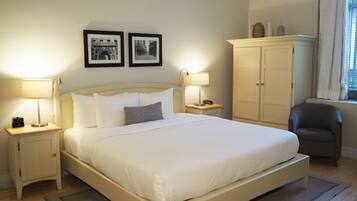 A neatly made bed with white linens, two bedside lamps, a nightstand with a clock, a wardrobe, and two framed pictures on the wall.