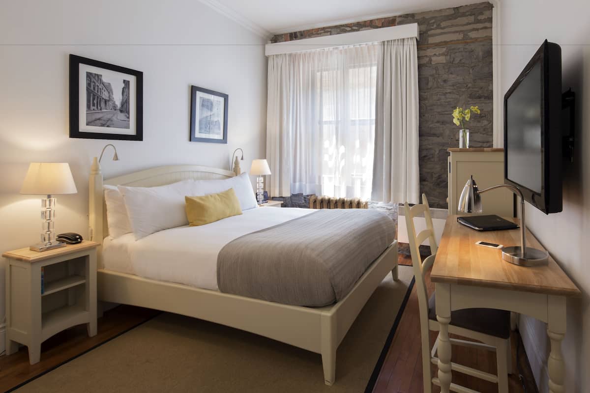 A hotel room with a bed, bedside tables, a desk, a chair, a television, and framed pictures on the wall.