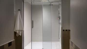 Una ducha moderna con puerta de vidrio, una toalla colgada en la pared y un pequeño estante con artículos de aseo.