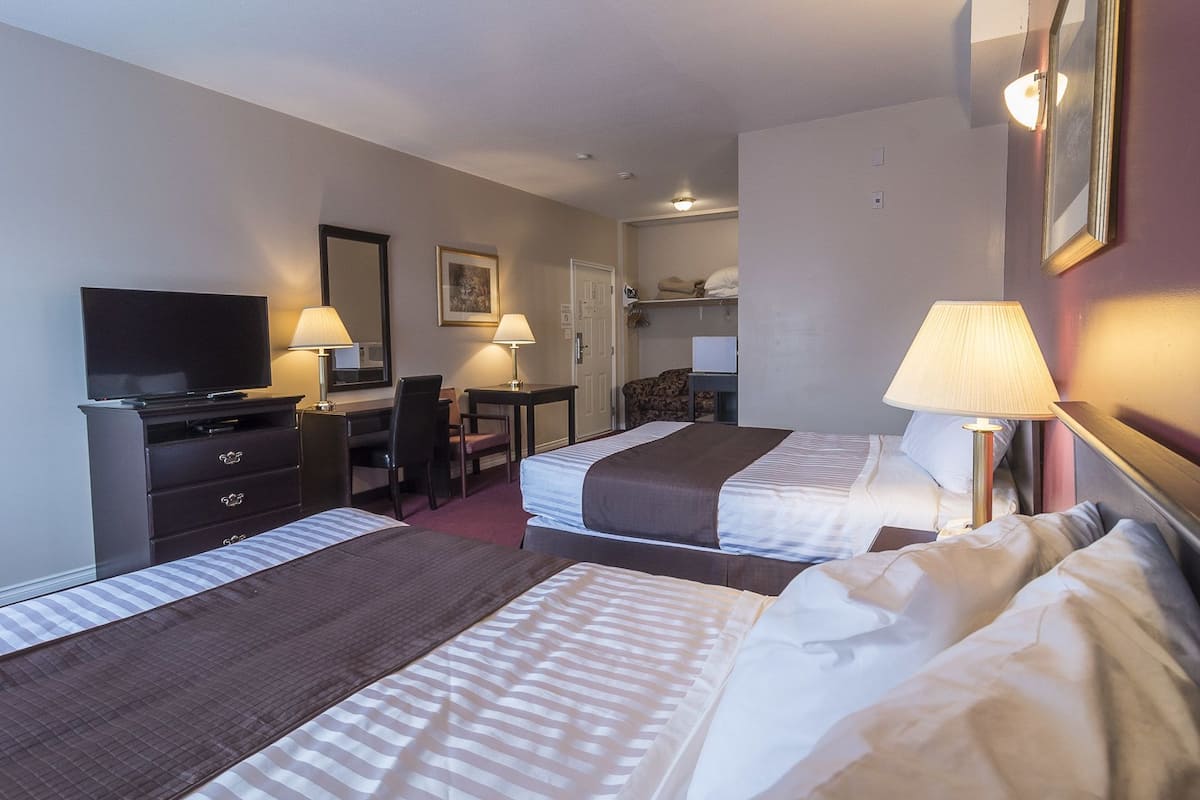 Habitación de hotel con dos camas, un escritorio, una silla, un televisor y una lámpara.