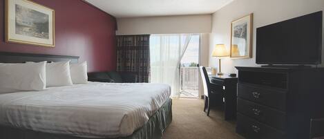 A hotel room with a bed, a desk, a television, and a balcony with curtains.