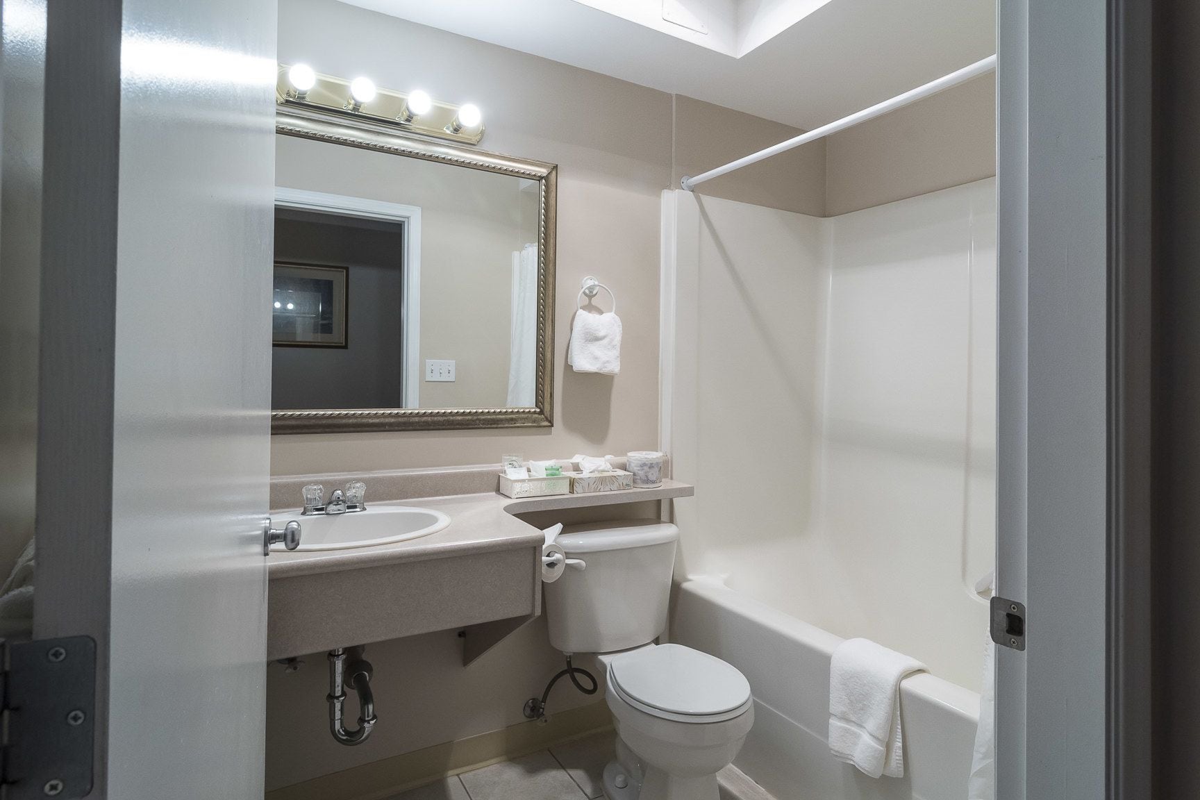 A bathroom with a sink, toilet, and shower. There is a mirror with lights above it.
