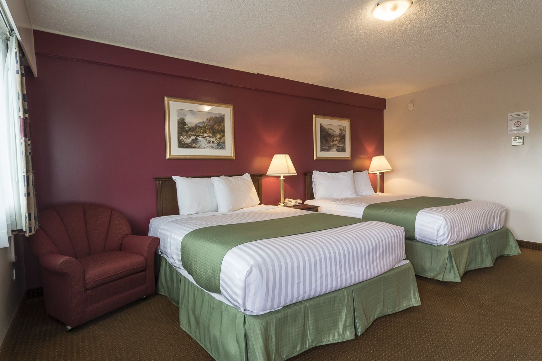 A hotel room with two beds, a chair, and two lamps.