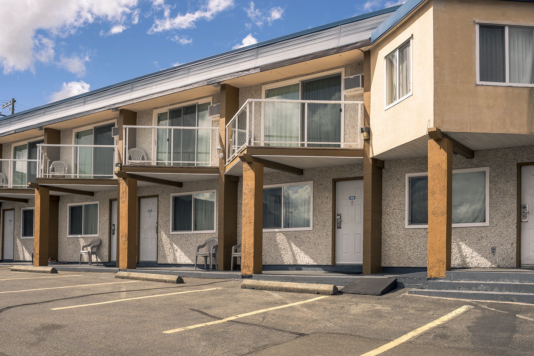 Une rangée de bâtiments d’un motel, dotés de nombreux balcons, de portes individuelles et d’un parking à l’avant.