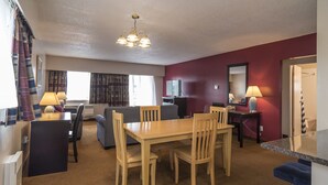 A hotel room with a dining area, a sofa, a TV, a mirror, and a bathroom visible through an open door. - Port Augusta Inn and Suites (Comox)