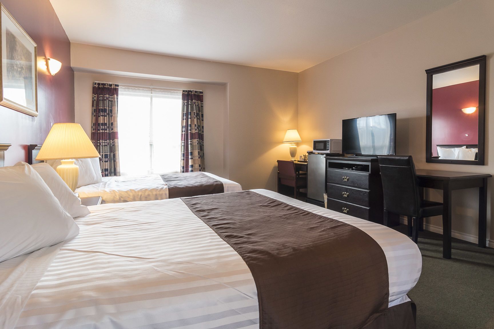 A hotel room with two beds, a desk with a computer, a television, and a window with curtains.