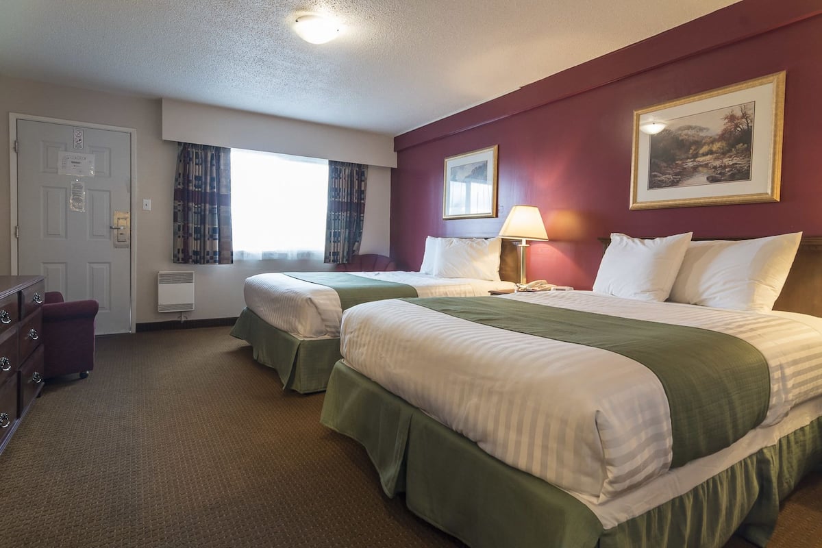Habitación de hotel con dos camas, un escritorio, una silla y una ventana con cortinas.