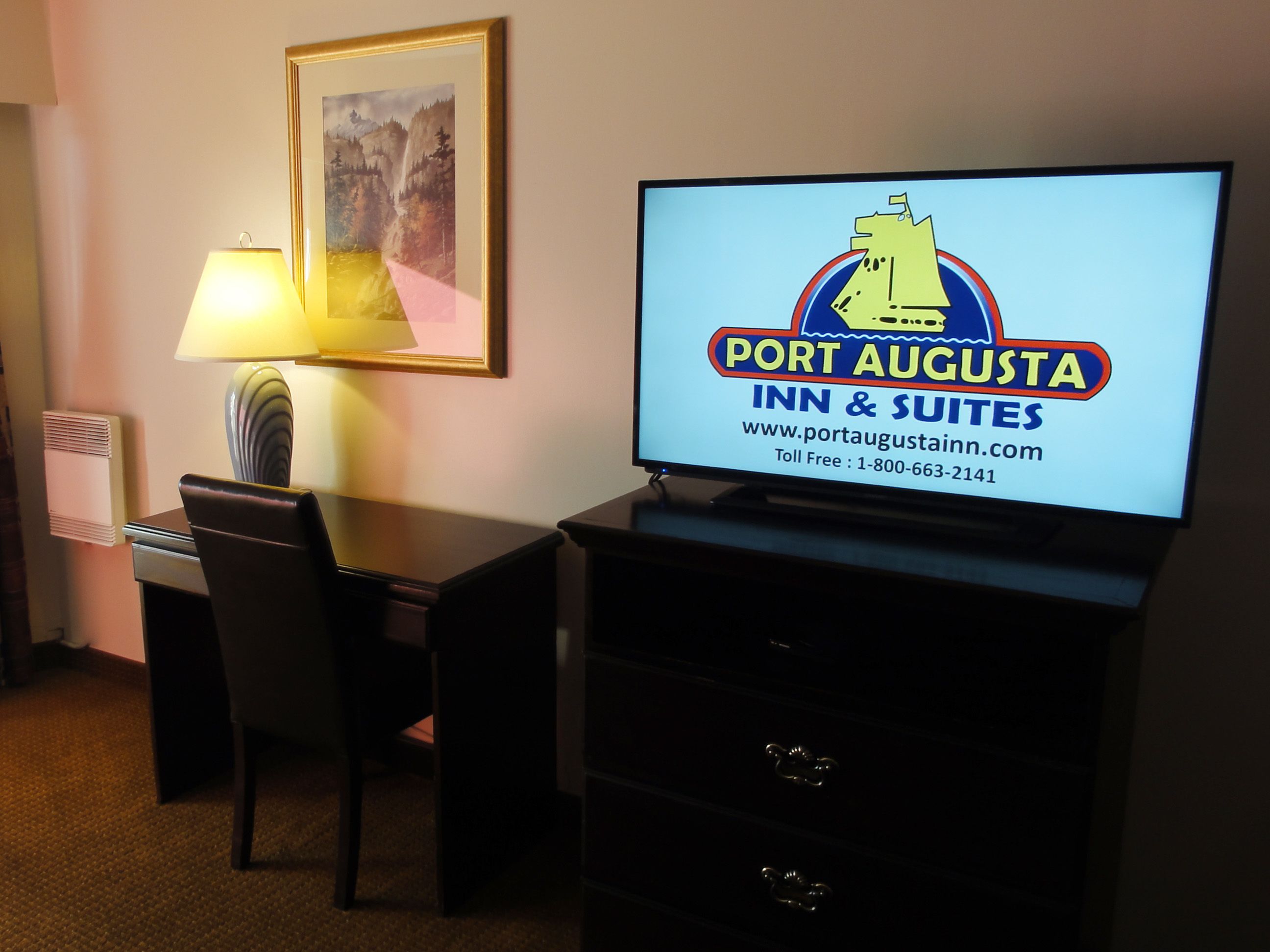 A hotel room with a desk, chair, and a television displaying the hotel's name and website.