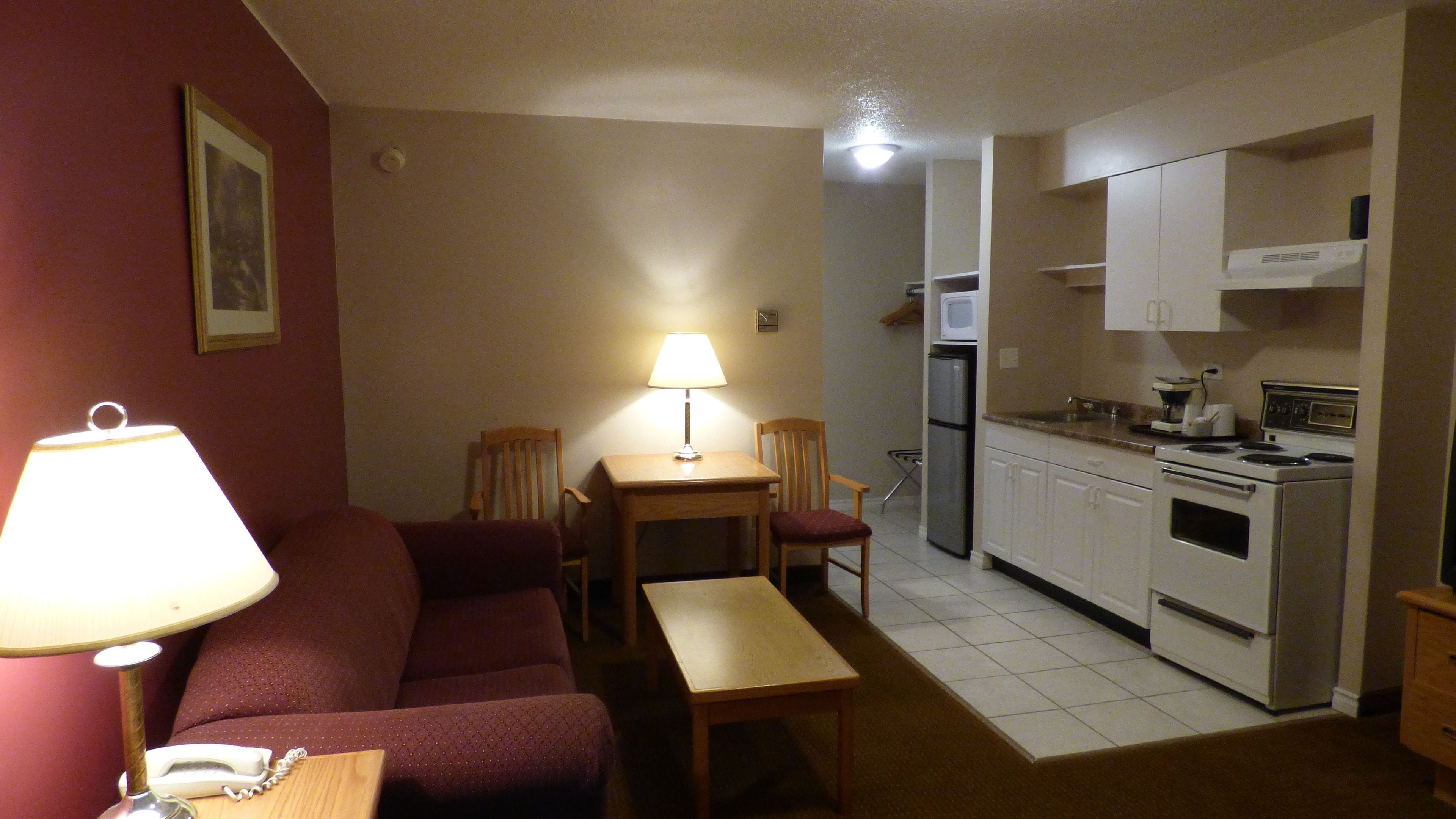 Un espace de vie compact comprenant un canapé, une petite table, une lampe, une chaise et une kitchenette équipée d’une cuisinière, d’un four à micro-ondes et d’un réfrigérateur.