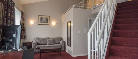 A living room with a sofa, a coffee table, a TV, and a staircase.