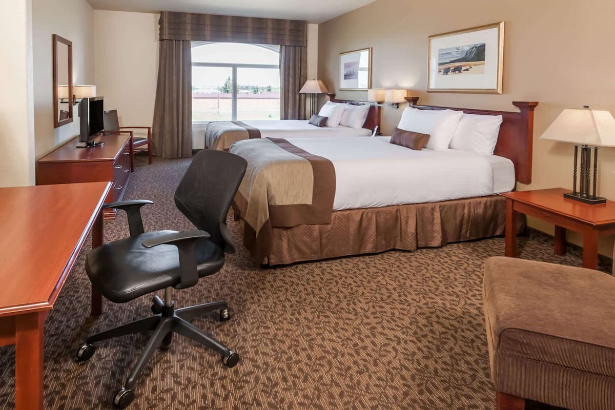 A hotel room with two beds, a desk, a chair, a TV, and a window with curtains.