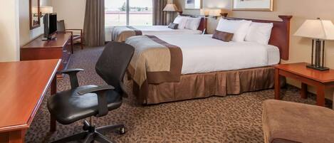 A hotel room with two beds, a desk, a chair, a TV, and a window with curtains.