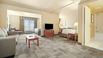 A hotel room with a sofa, a TV, a desk, a lamp, and a bathroom visible through an open door.