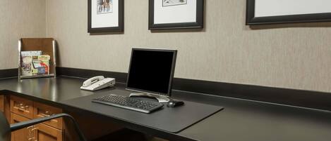 A hotel reception desk with a computer, phone, and framed artwork on the wall.