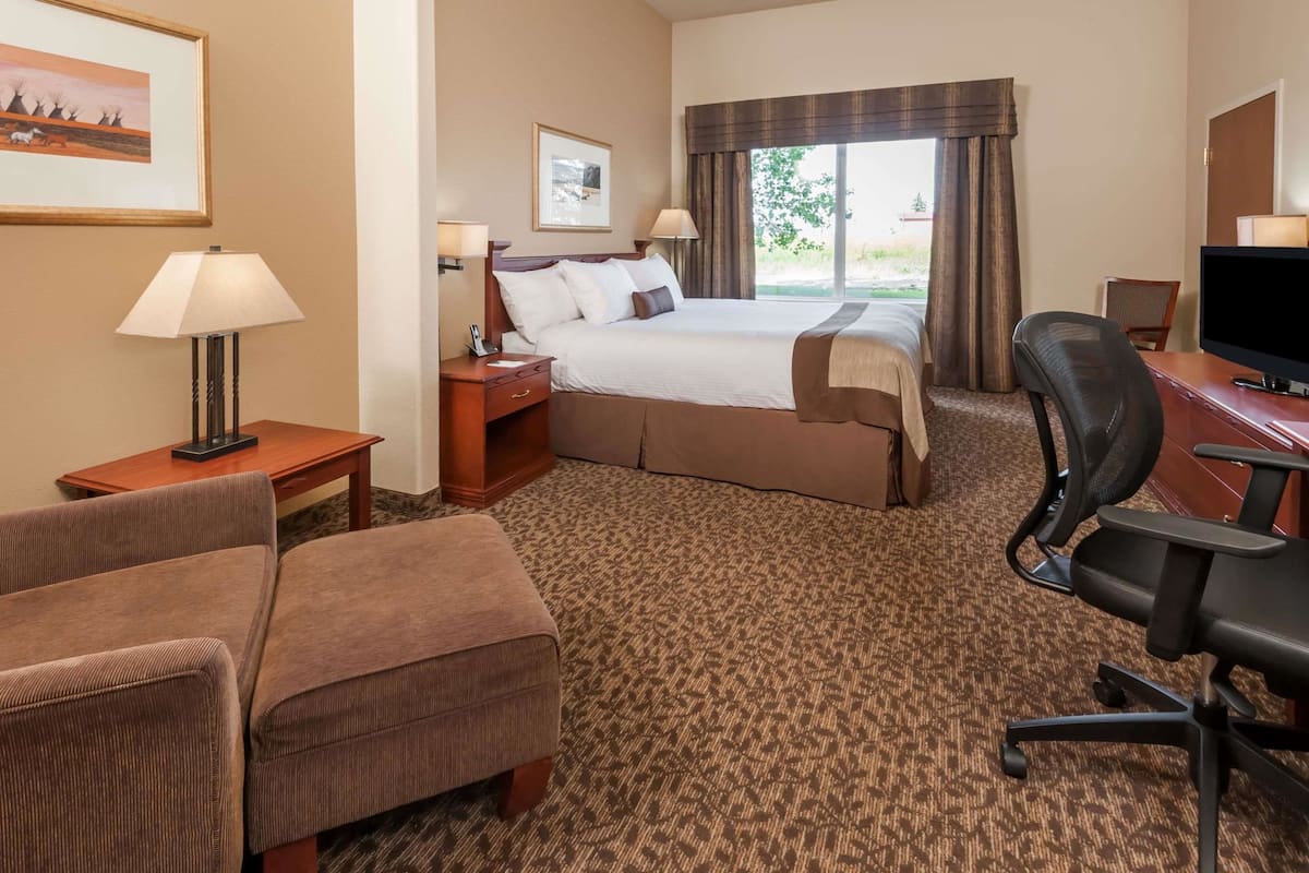 A hotel room with a large bed, a desk with a chair, a TV, a lamp, and a carpeted floor.