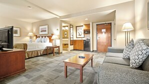 Una habitación de hotel con cama, sofá, escritorio, televisor y kitchenette.
