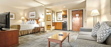 A hotel room with a bed, a sofa, a desk, a TV, and a kitchenette.