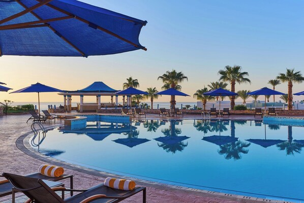 A pool area with lounge chairs, umbrellas, and palm trees.