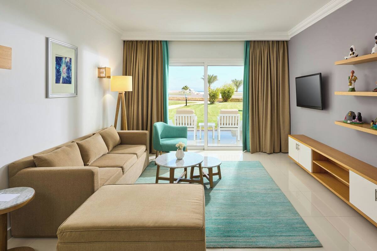 Un salon moderne avec un canapé, une petite table, un téléviseur et un balcon aménagé avec du mobilier d’extérieur.