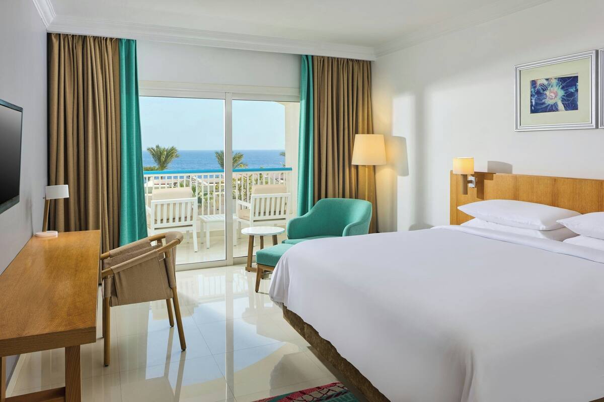 Une chambre d’hôtel comprenant un lit, un bureau, une chaise, un balcon avec vue sur l’océan et une télévision.
