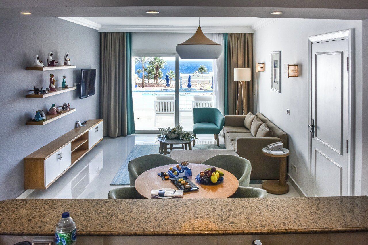 A modern hotel room with a balcony, a seating area with a round table, and a TV mounted on the wall.