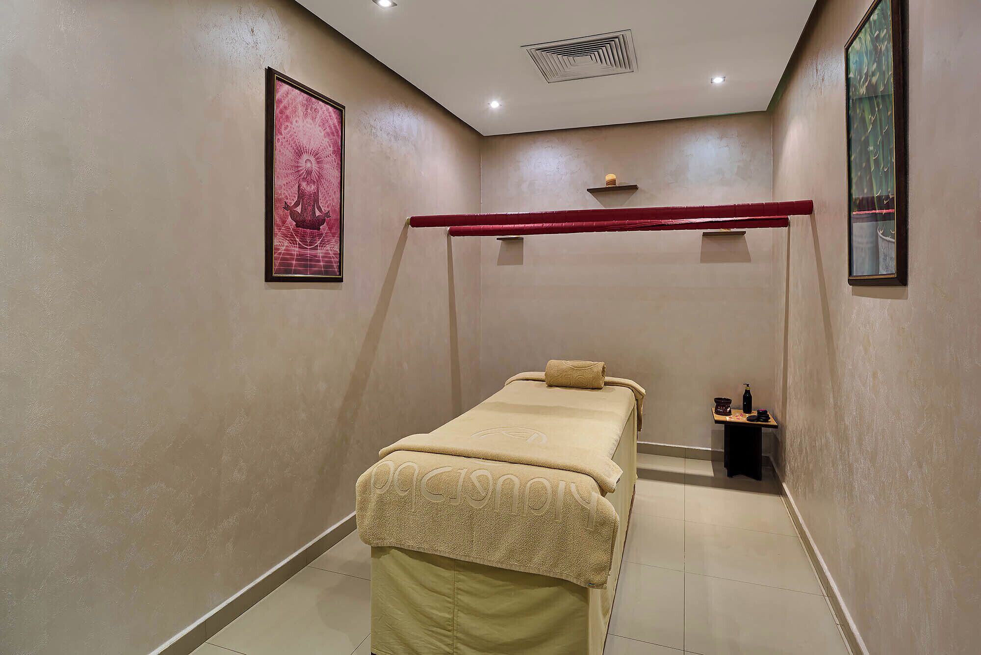 A small, private room with a single bed, a small table with a bottle and a cup, and a framed picture on the wall.